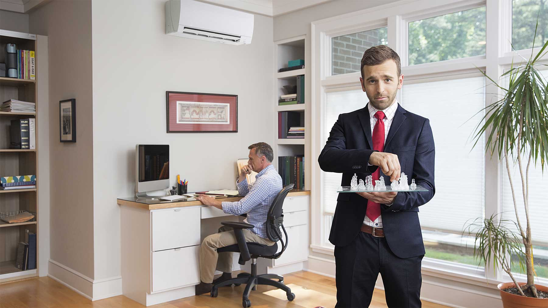 Mitsubishi Electric spokesperson holding a chessboard while standing in a home office with a Mitsubishi Electric ductless air conditioner