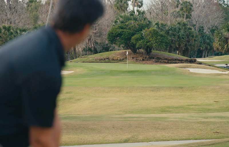 back of golfer's head staring at the green